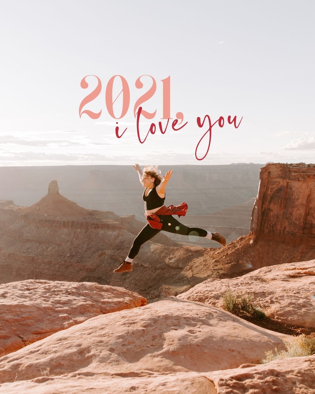 A gleeful woman leaps across a gap in a canyon within Canyonlands National Park, and the words "2021, I Love You" are painted across the sky in pink and red type.